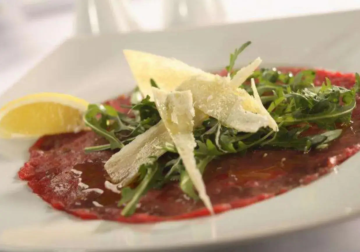 Eleganckie carpaccio wołowe z rukolą, parmezanem i cytryną. Jak jeść? Delikatnie, by docenić smak.