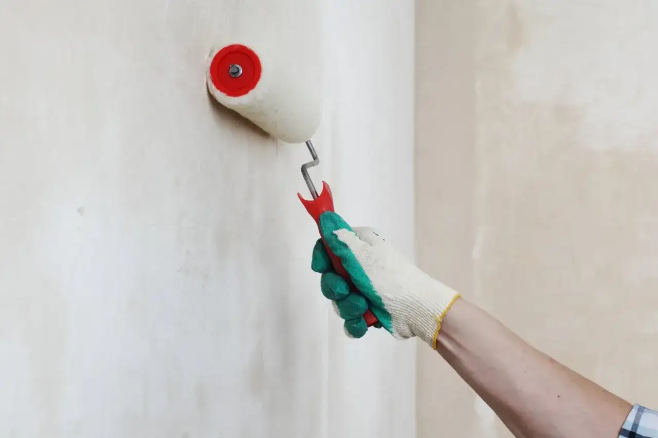 Mano guantata stende la primer vernice su un muro grezzo con un rullo.