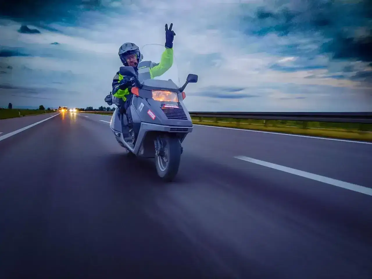 Motocyklista na skuterze 125 z podniesioną ręką pozdrawia, jadąc po autostradzie. Czy motocyklem 125 można jeździć po autostradzie? Tak!