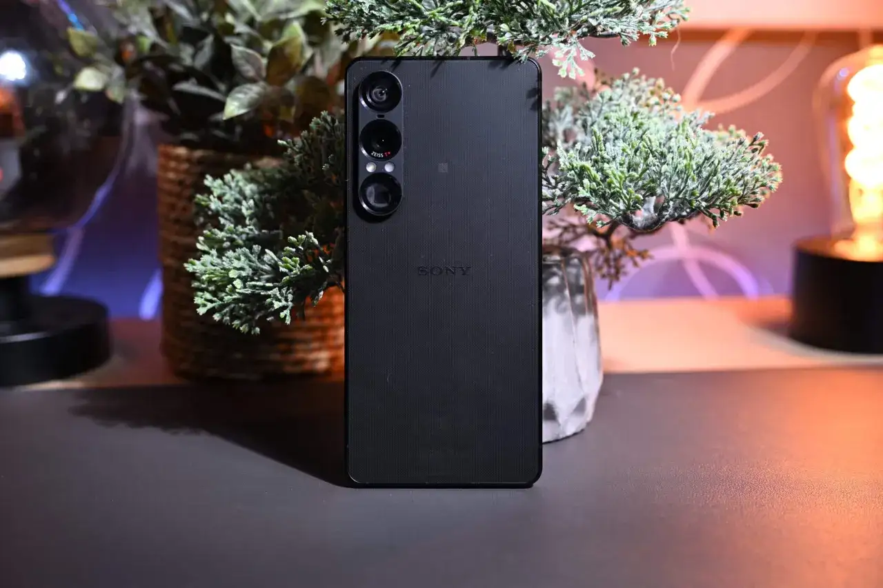 Czarny smartfon Sony Xperia XZ4 z potrójnym aparatem, otoczony zielenią i ciepłym światłem.