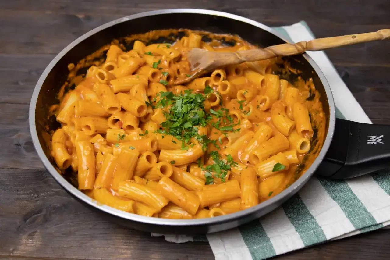 Herzhafte Rigatoni in cremiger **Tomaten Sahne Sauce**, garniert mit frischer Petersilie, bereit zum Servieren in einer Pfanne.