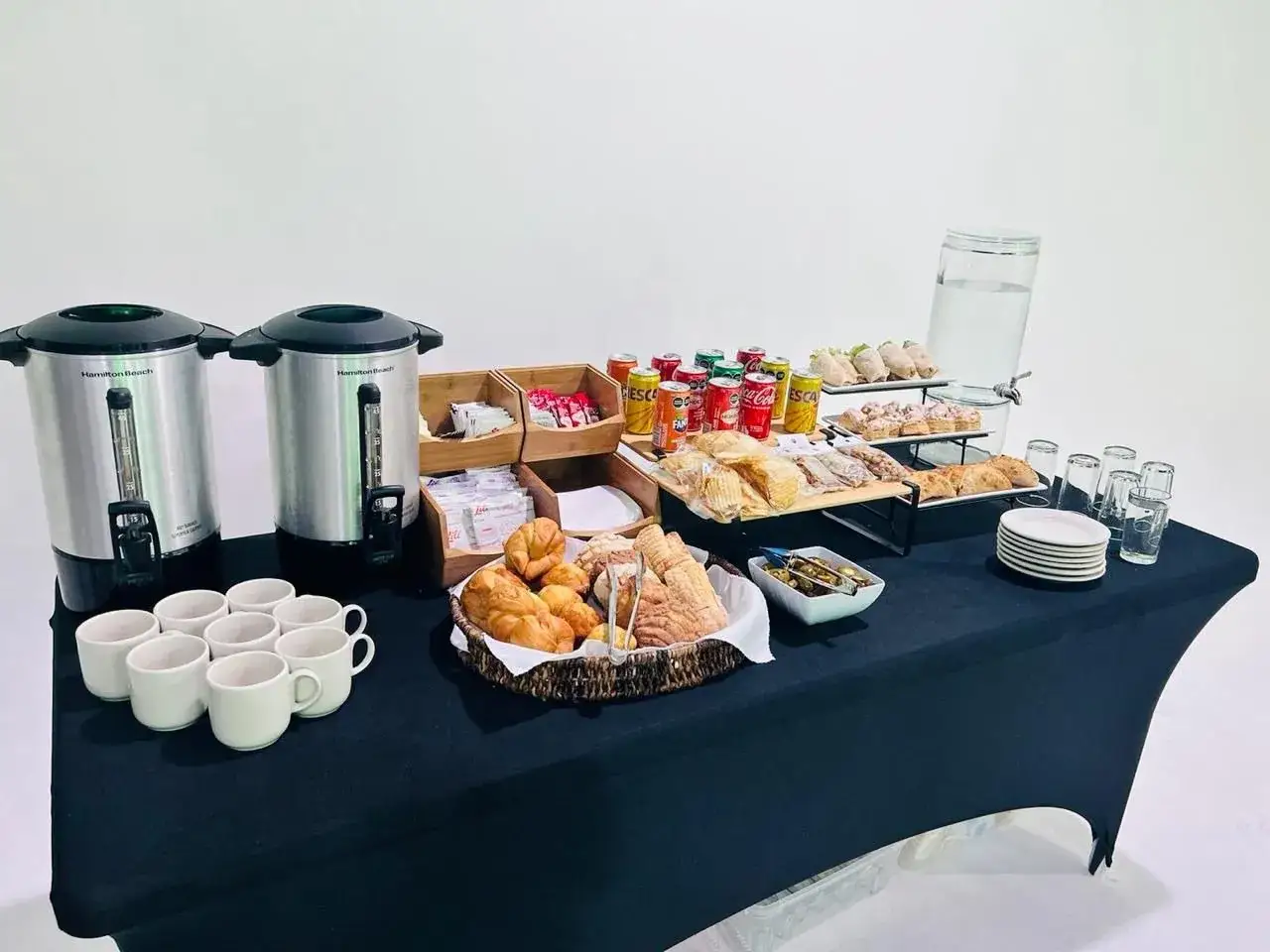 Montaje coffee break con dispensadores de caf&eacute;, tazas, boller&iacute;a, s&aacute;ndwiches, patatas fritas y bebidas.