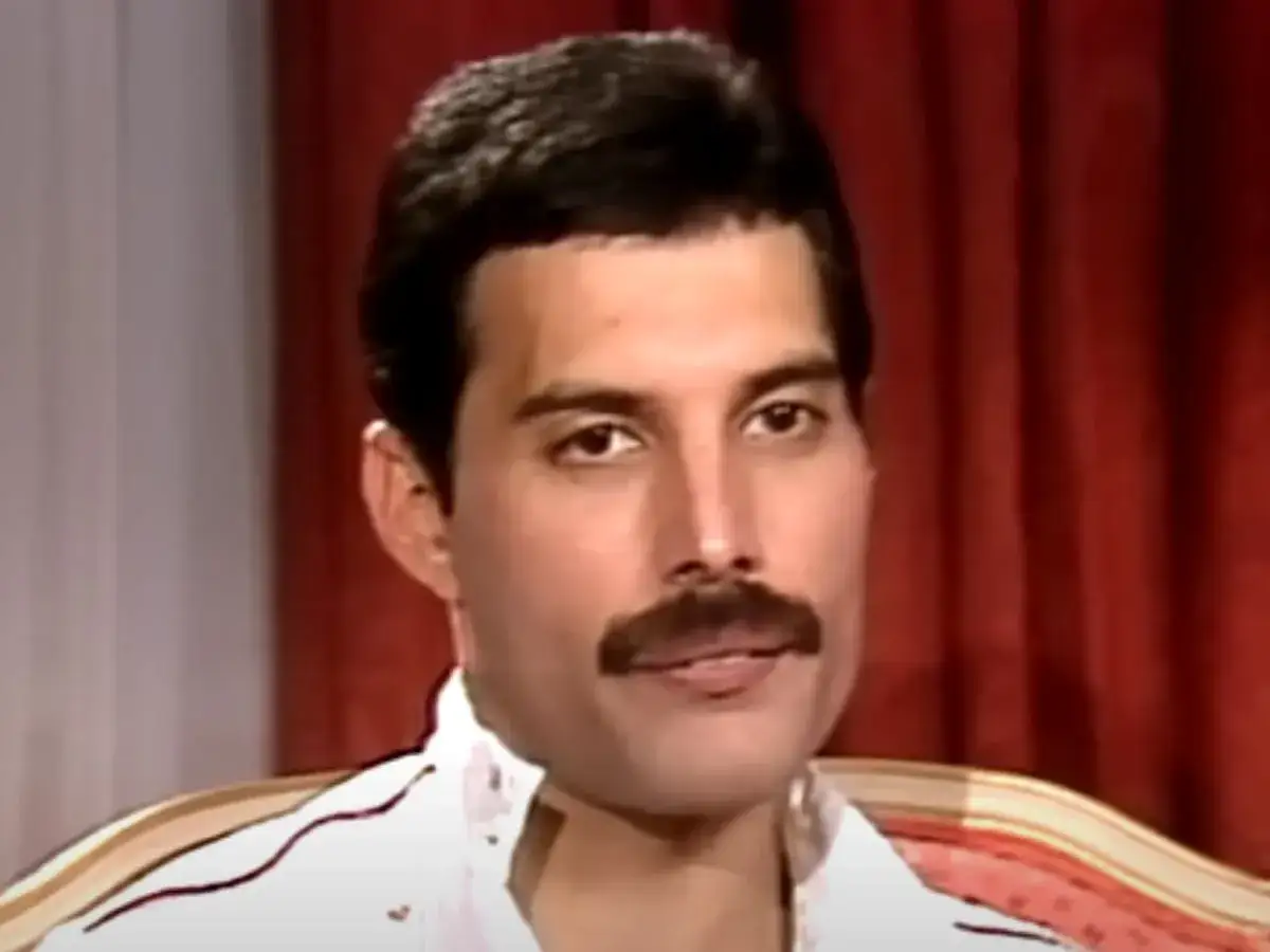 Freddie Mercury z charakterystycznym wąsem, w białej koszuli. Choć nie ma dzieci, jego muzyka żyje w sercach fanów.