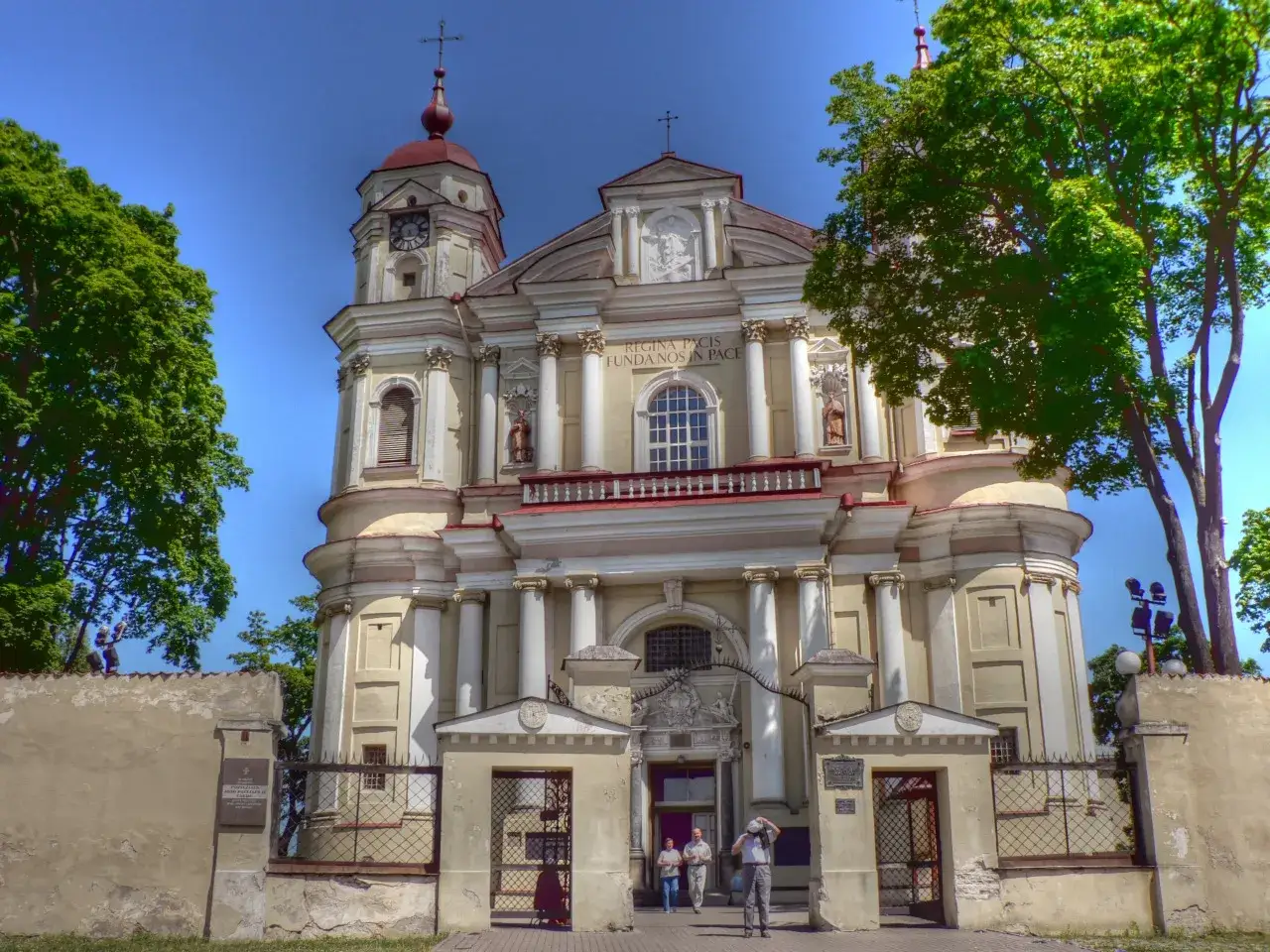 Barokowy kościół w Wilnie, jeden z pięknych kościołów wileńskich, z wieżą zegarową i zielonymi drzewami.