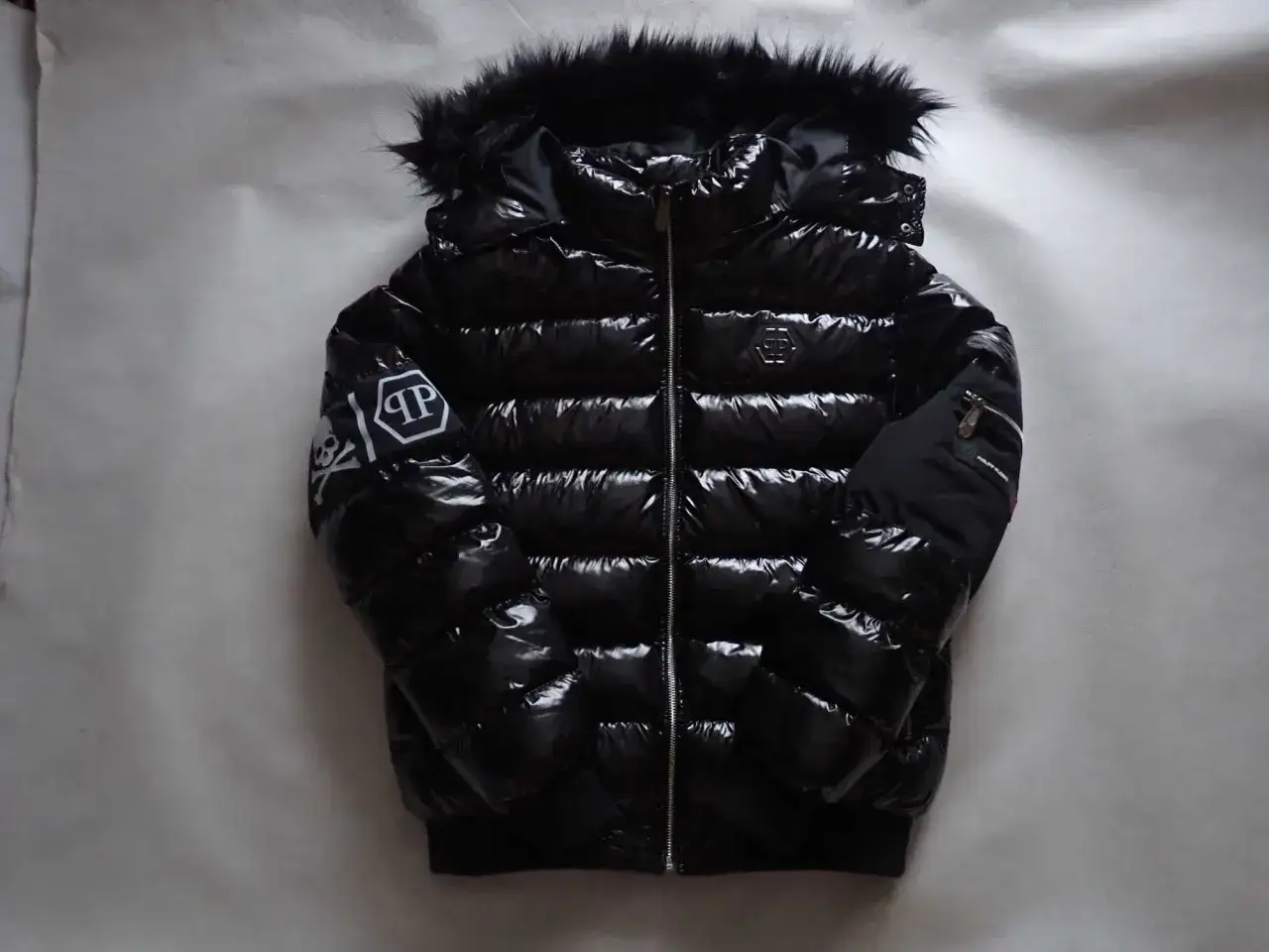 Błyszcząca, czarna kurtka puchowa z futrzanym kapturem. Na rękawie widoczne logo Philipp Plein.