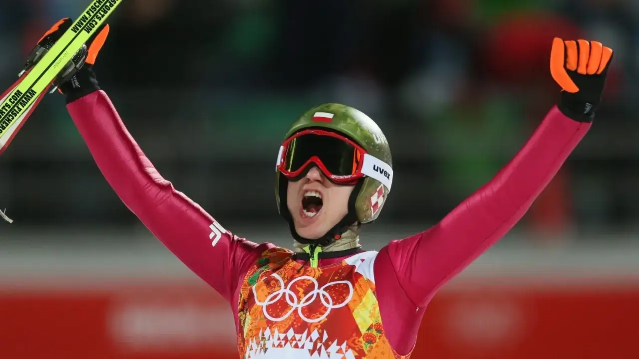 Skoczek narciarski w barwach narodowych, z uniesionymi rękami, świętuje sukces. To nadzieja na medal dla reprezentacji Polski na zimowe igrzyska olimpijskie 2026.