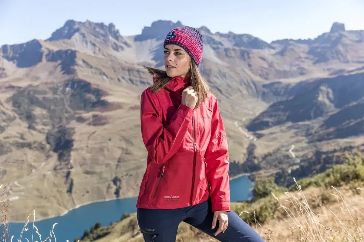 Mujer con gorro y chaqueta hardshell roja, lista para la aventura en la monta&ntilde;a.