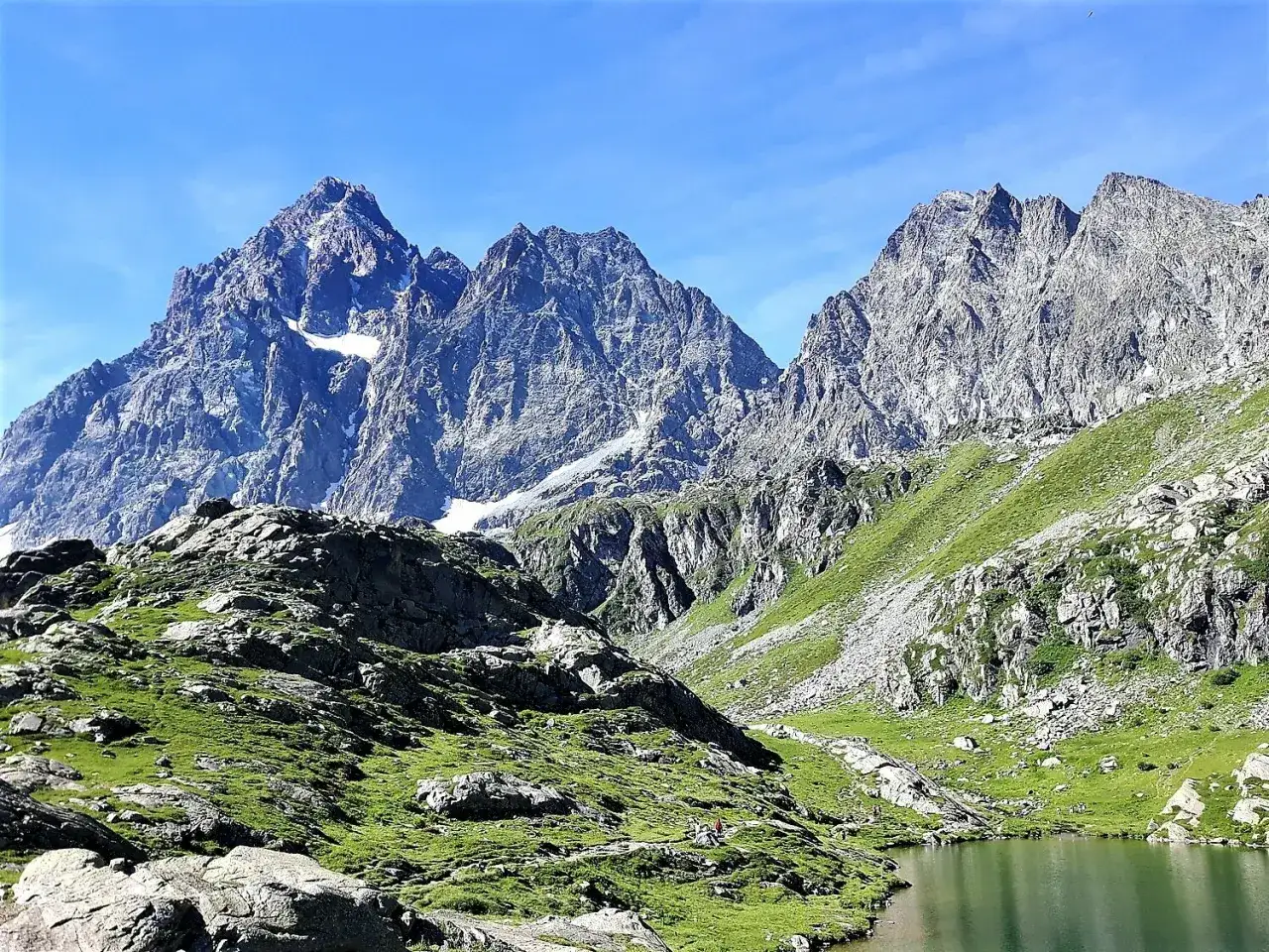 Un lago alpino riflette montagne imponenti e prati verdi. Un luogo ideale tra i **posti da visitare in Piemonte** per immergersi nella **natura** incontaminata.