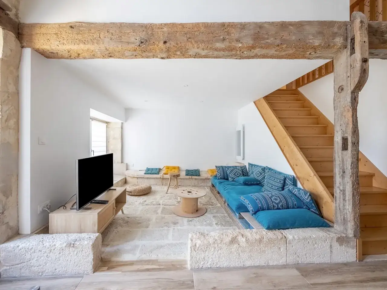 Salon moderne dans une grange rénovée. Le prix de la rénovation grange inclut poutres apparentes, escalier bois, canapé bleu, TV.