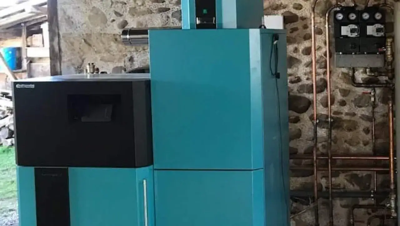 Chaudière à granulés avis : installation moderne et efficace dans une chaufferie en pierre. Tuyauterie en cuivre et tableau de contrôle visible.