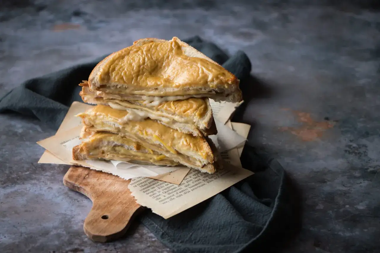 Pile de croque monsieur v&eacute;g&eacute;tarien dor&eacute;s, servis sur des pages de livre anciennes, sur une planche en bois.
