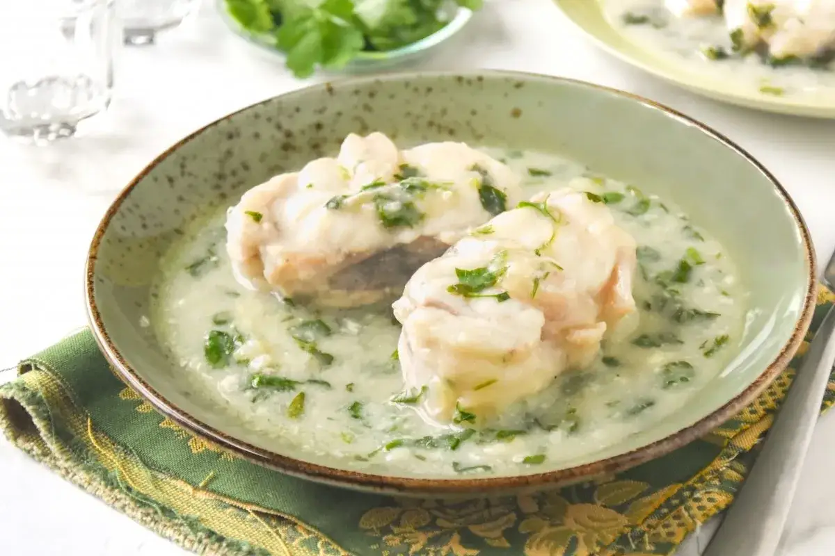 Dos albóndigas de rape en una cremosa salsa verde con perejil picado, servidas en un cuenco rústico.