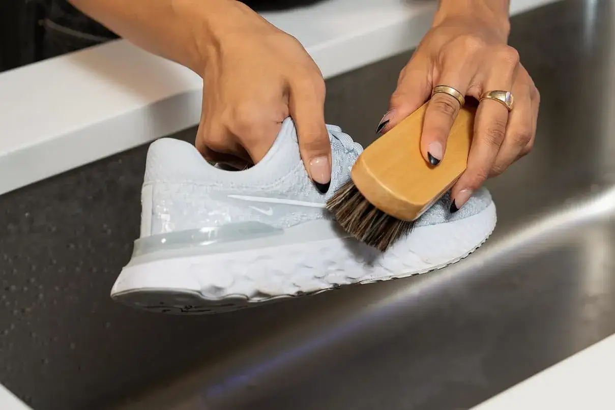 Manos cepillando zapatilla blanca en el lavabo, un paso clave para saber como lavar zapatillas blancas y que no queden amarillas.