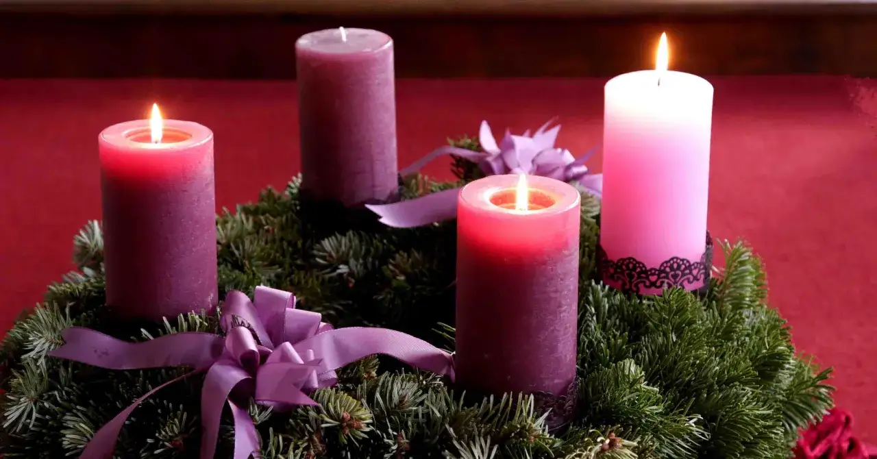 Drei brennende Kerzen auf einem Adventskranz aus Tannengrün mit lila Schleifen. Der dritte Advent ist da!