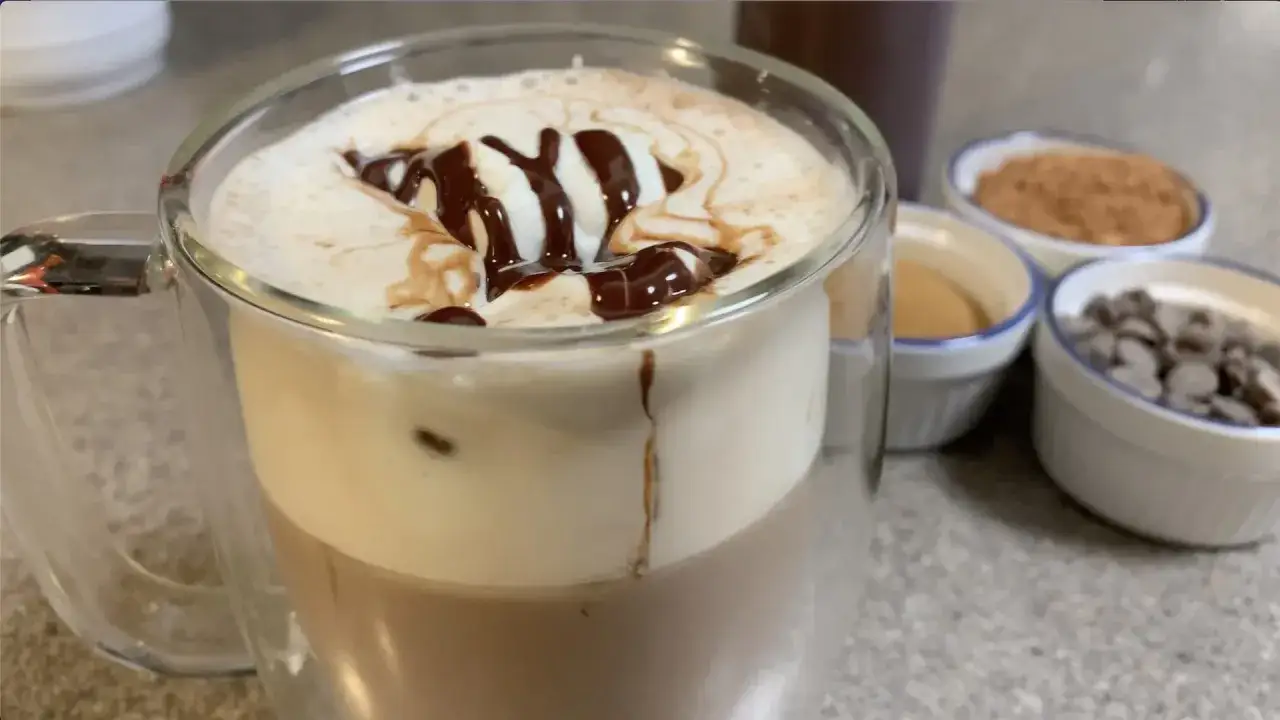 Ein köstlicher Caffè Mocca mit Sahne und Schokoladensirup, daneben kleine Schälchen mit Kakaopulver, Zucker und Schokostückchen.