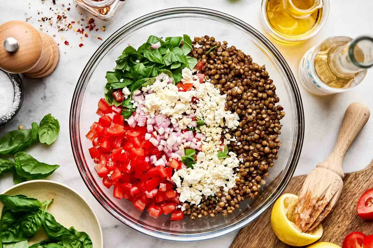 Bunter Salat mit Linsen, Tomaten, roten Zwiebeln, Feta und Spinat. Ein Zitronenpresse liegt daneben.