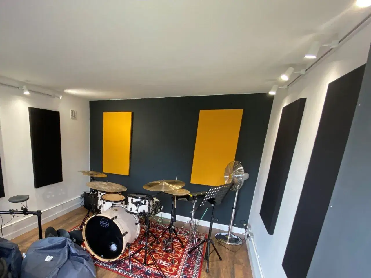 Batterie sur un tapis rouge, avec des panneaux acoustiques jaunes et noirs sur les murs. Le placement batterie est id&eacute;al pour l'enregistrement.