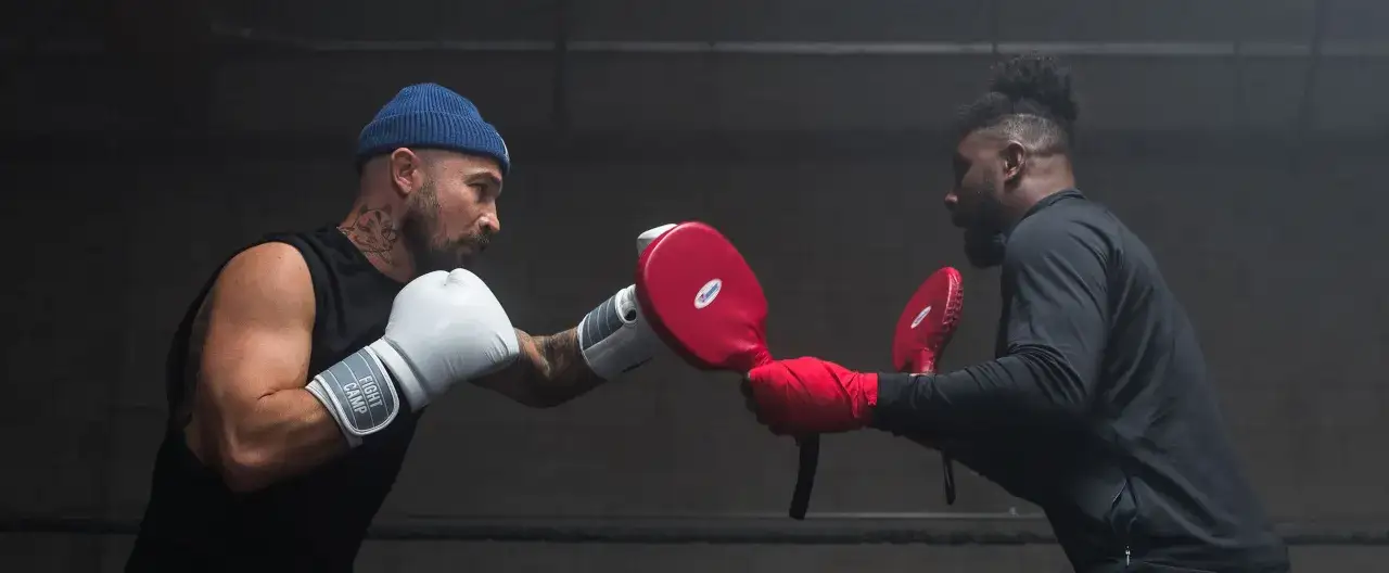 Two boxers in a ring. One throws a punch, the other holds pads. This shows the boxer puncher meaning in action.