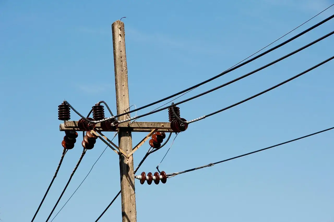 Słupy energetyczne z izolatorami i przewodami na tle błękitnego nieba. Zastanawiasz się, ile można dostać odszkodowania za słupy energetyczne?