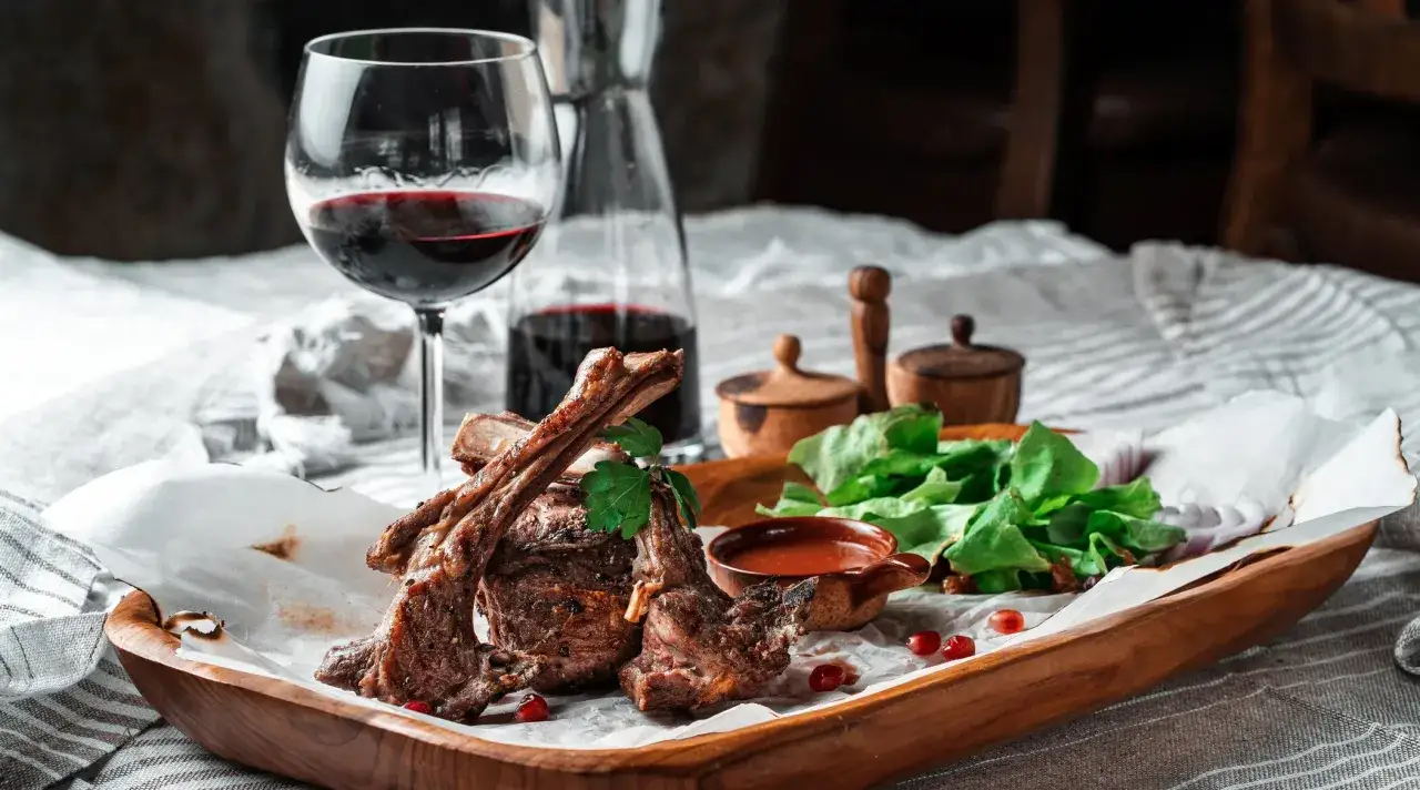 Saftige Lammkoteletts mit frischem Salat und einem Glas Rotwein. Die perfekte Wahl, welcher Wein zu Lamm passt, ist oft ein kräftiger Rotwein.