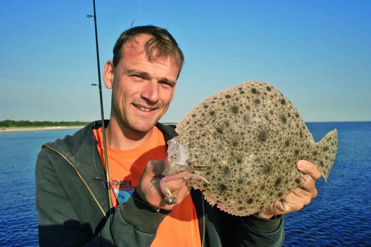 Gl&uuml;cklicher Angler h&auml;lt stolz einen frisch gefangenen Steinbutt in der Ostsee.
