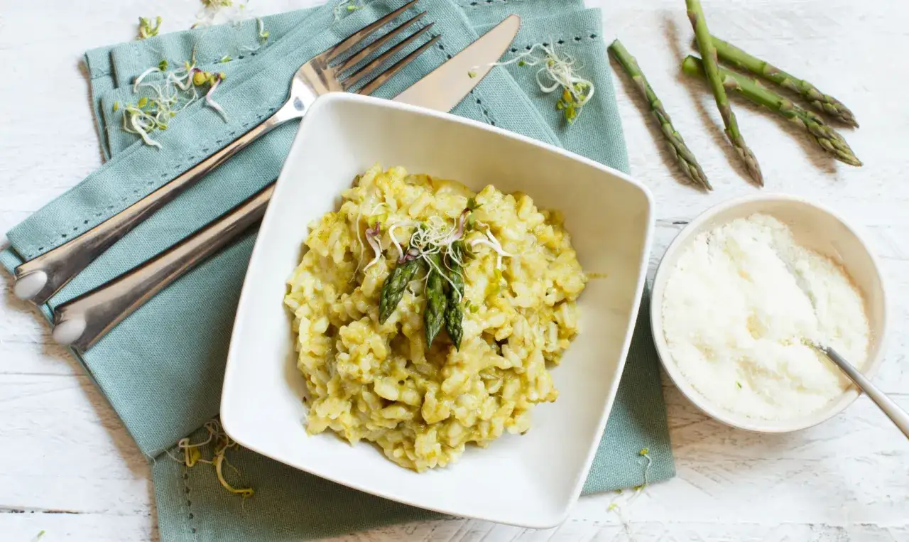 Un crémeux risotto aux asperges, garni de pousses et servi avec du parmesan râpé. Parfait pour un repas léger.