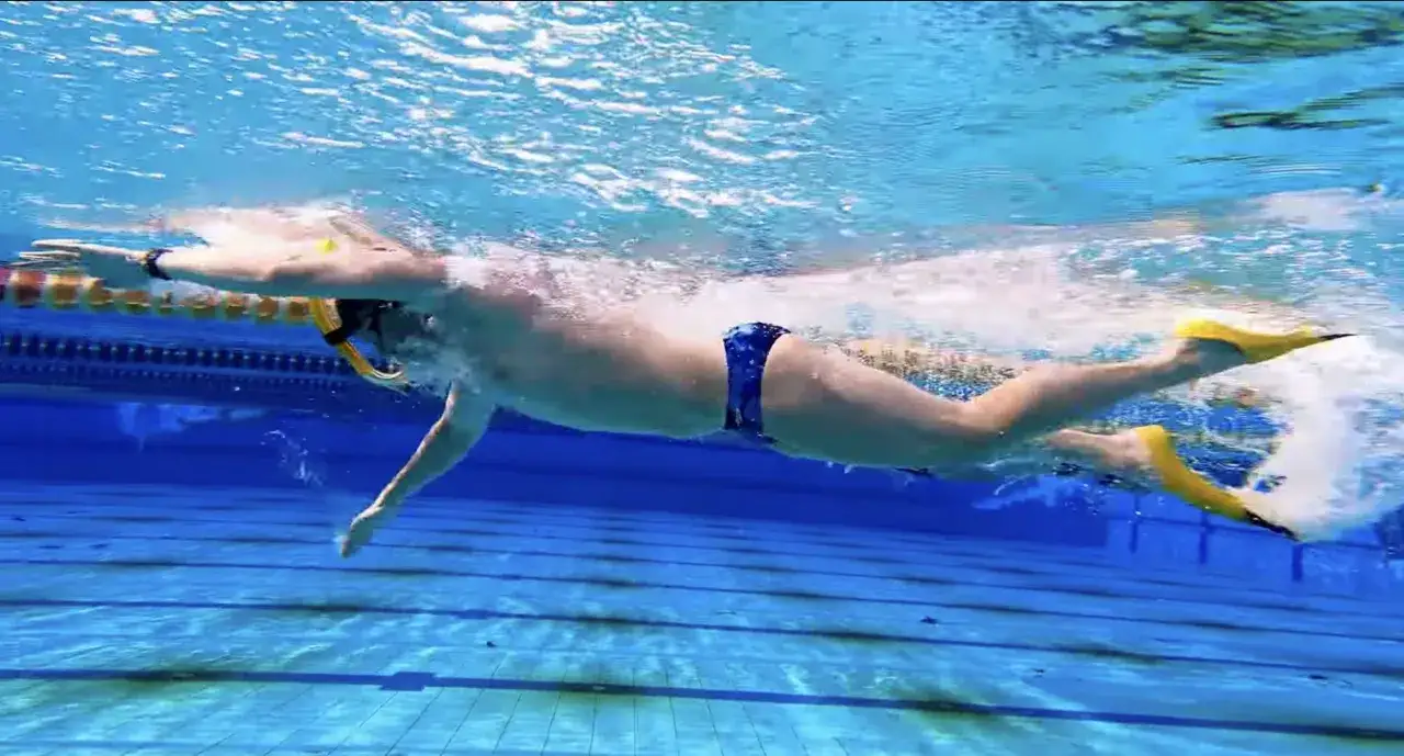 Schwimmer mit Schnorchel und Flossen gleitet durch das Wasser. Die gelben Flossen treiben ihn voran, während er mit den Armen paddelt.