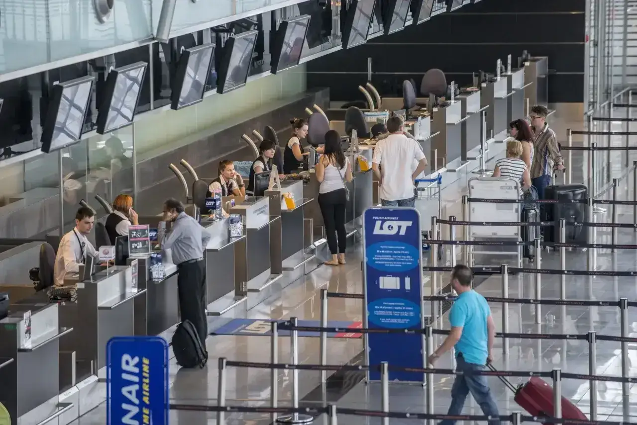 Odprawa celna na lotnisku w toku. Pasażerowie z bagażami czekają w kolejce do stanowisk LOT Polish Airlines.