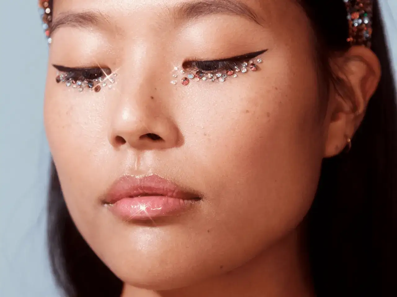 En närbild på en ung kvinna med glittrande ögonlock och en skarp eyeliner. Hon har en glansig läppglans och en gnistrande tiara.