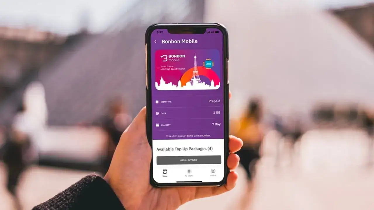 Une main tient un smartphone affichant une application pour acheter un forfait de données eSIM pour l'internet à l'étranger, avec la Tour Eiffel en arrière-plan.