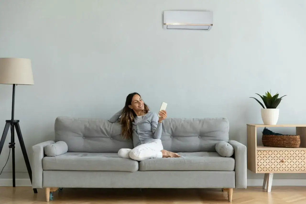 Mujer sonr&iacute;e en el sof&aacute;, disfrutando del aire acondicionado a 27 grados en verano.