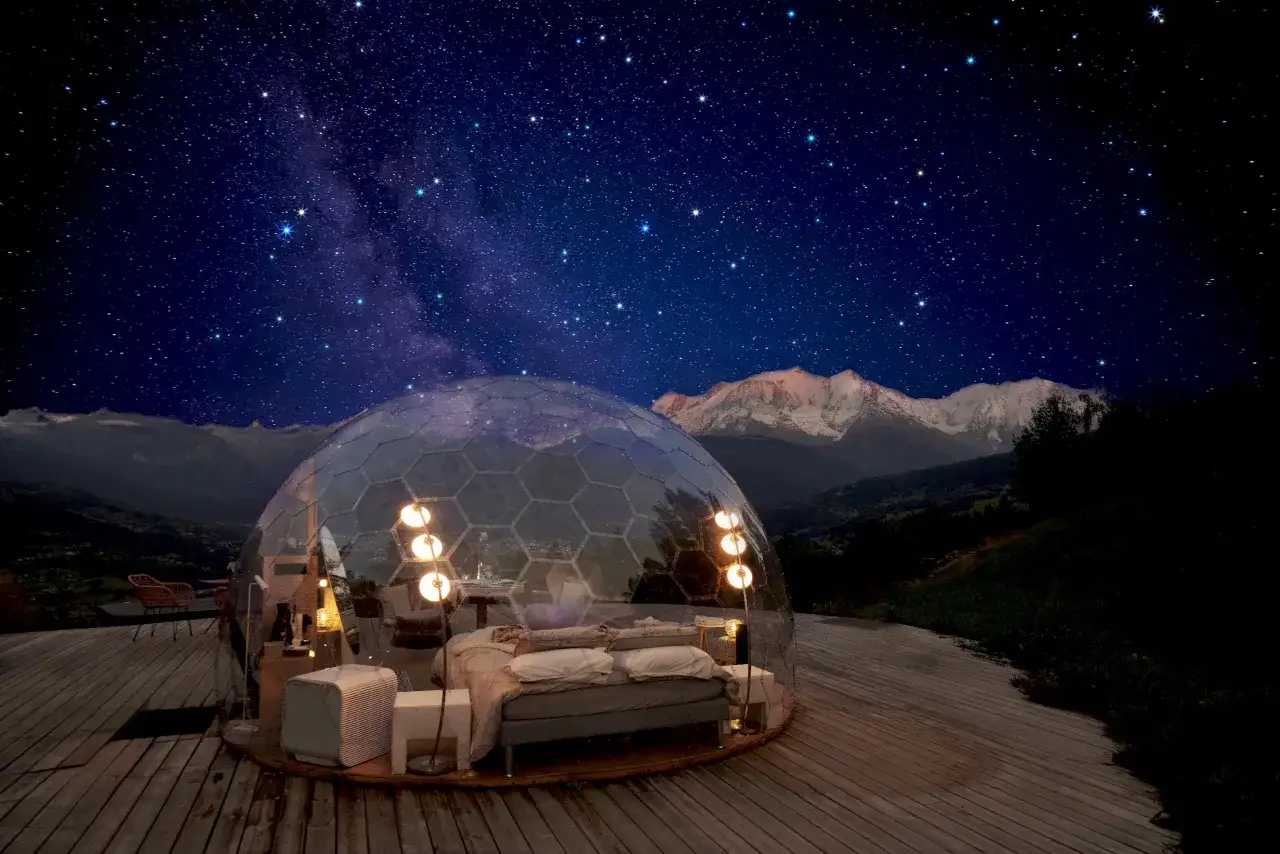 Une bulle transparente offre un lit douillet sous un ciel étoilé. Une nuit bulle inoubliable avec vue sur les montagnes.