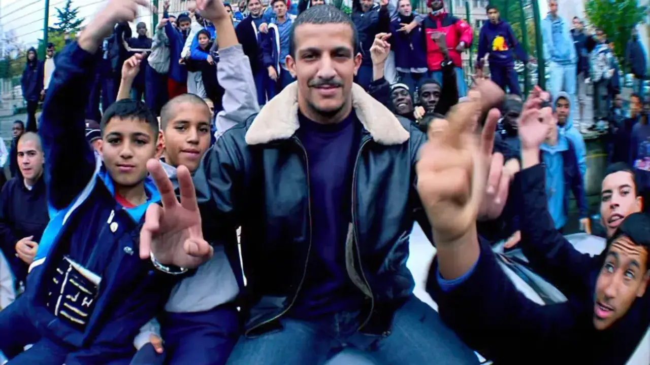 Un groupe de jeunes, dont un homme au centre en blouson de cuir, célèbre l'énergie du rap francais.