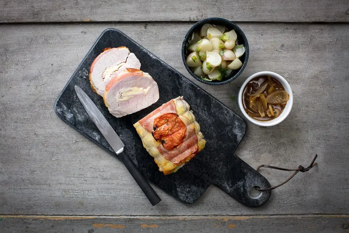 Rôti de porc Orloff, tranché, servi avec des légumes et une sauce aux oignons sur une planche en marbre.