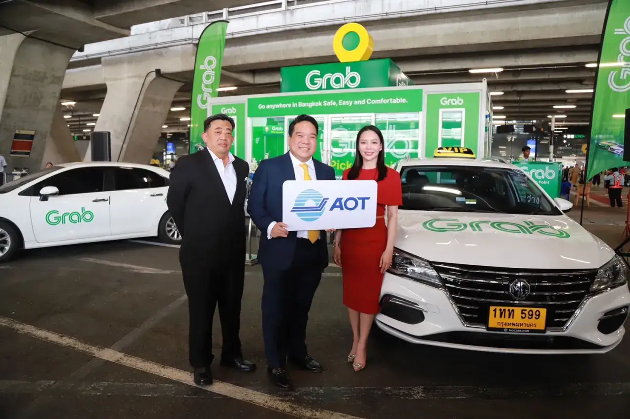 Drei Personen posieren vor einem Grab-Taxi und einem Grab-Stand. Ein Mann h&auml;lt ein AOT-Schild. Dies ist ein Event f&uuml;r Grab in Thailand.