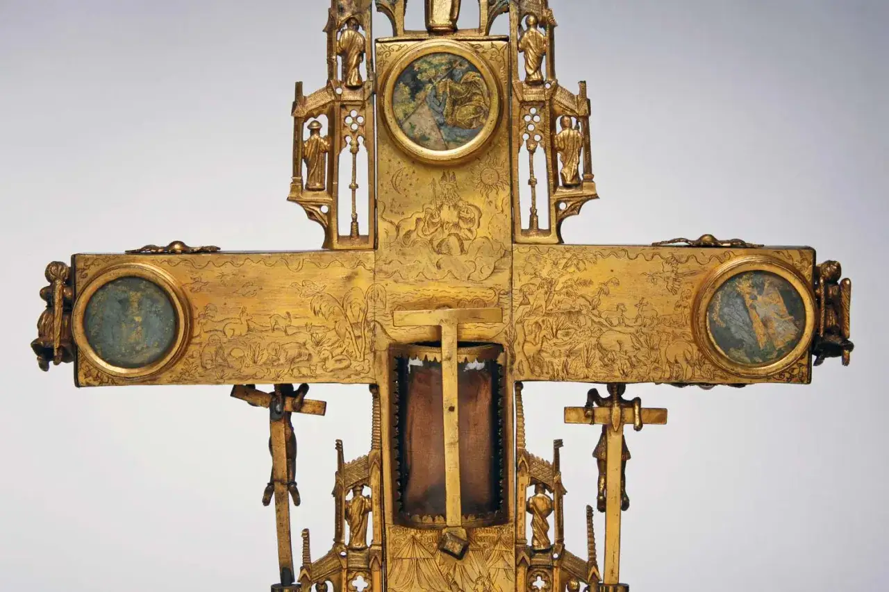 Ornate golden reliquary cross, depicting biblical scenes and figures, with a central compartment possibly holding a holy body.