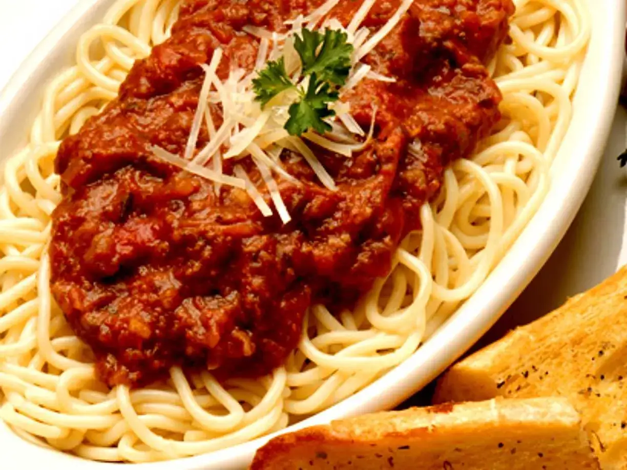 En portion spaghetti med en mustig k&ouml;ttf&auml;rss&aring;s, toppad med riven ost och persilja. Serveras med rostat vitl&ouml;ksbr&ouml;d. En klassisk pasta bolognese.