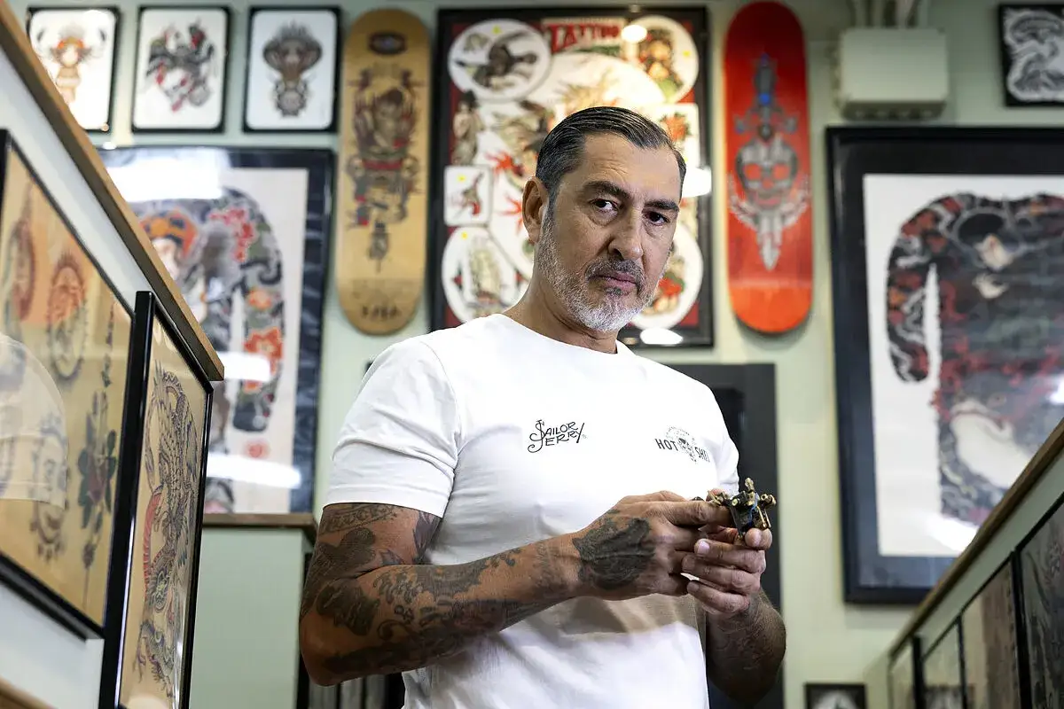 El mejor tatuador del mundo, con su m&aacute;quina en mano, rodeado de arte en skateboards y tatuajes tradicionales.