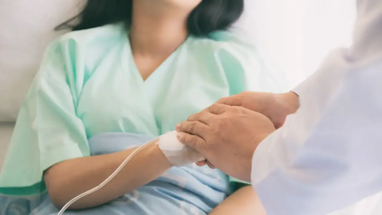 Dłoń lekarza pociesza pacjentkę w szpitalnym łóżku, która przeżywa trudne chwile po poronieniu.
