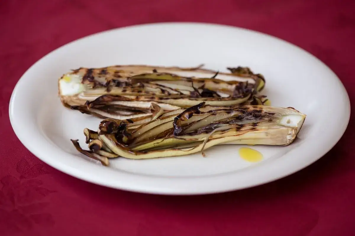 Radicchio in padella, leggermente caramellato e condito con olio d'oliva, servito su un piatto bianco.