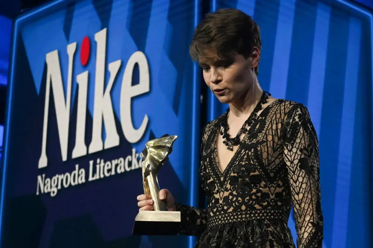 Kobieta w czarnej koronkowej sukni odbiera nagrodę literacką Nike.