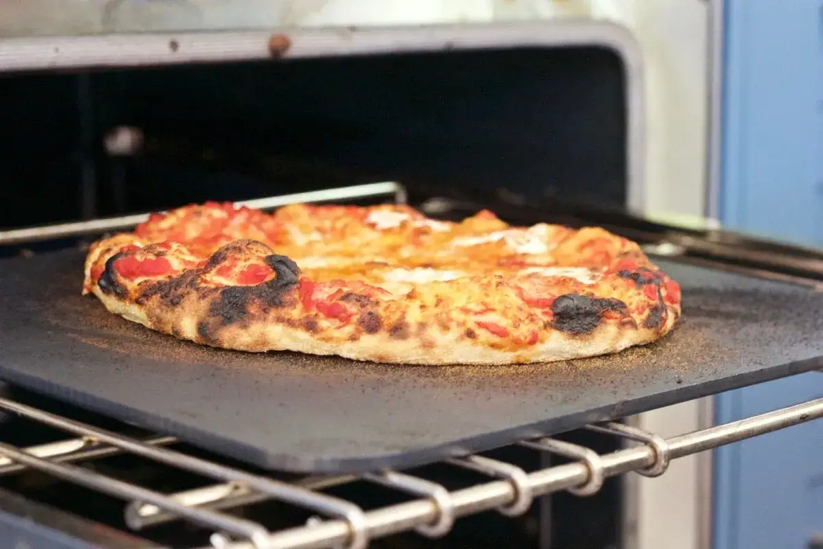 Une pizza en pleine cuisson sur une pierre, le fromage dor&eacute; et la cro&ucirc;te l&eacute;g&egrave;rement br&ucirc;l&eacute;e promettent un d&eacute;lice.