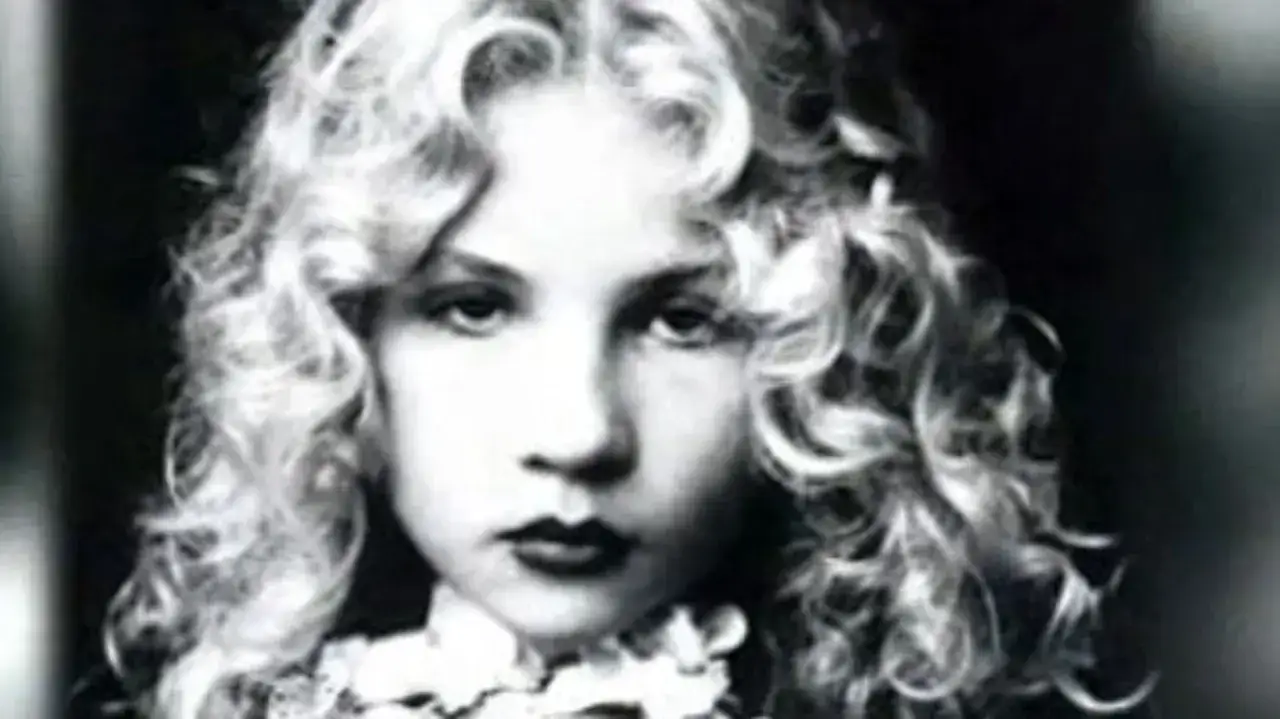 Portrait en noir et blanc d'Eva Ionesco enfant, aux boucles blondes et au regard intense, une jeune fille à l'aura mystérieuse.