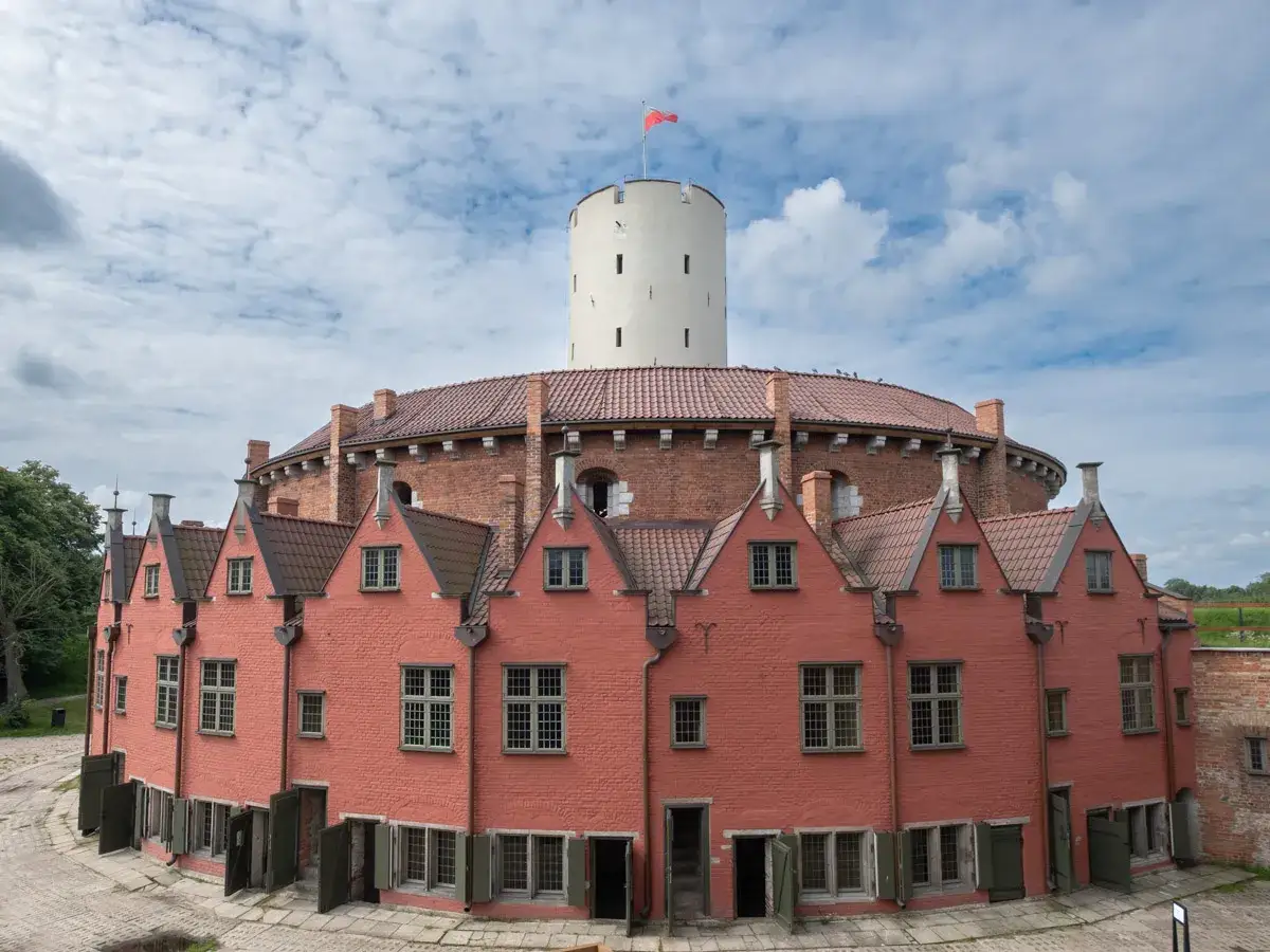 Okazała twierdza z cegły z charakterystyczną wieżą, oferująca nietypowe atrakcje w Gdańsku.