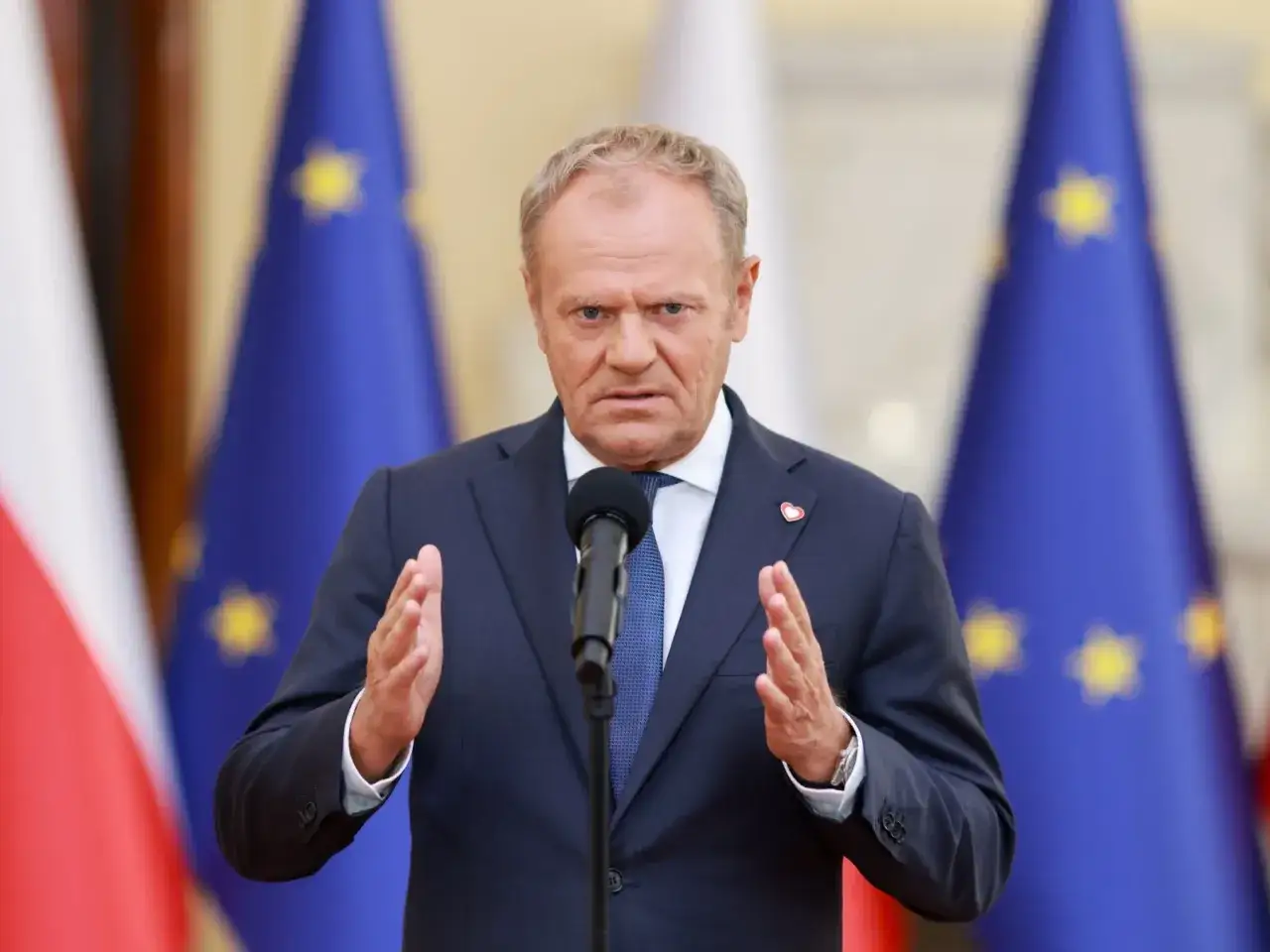 Donald Tusk z uniesionymi dłońmi, przemawia na tle flag Polski i UE. Czy to wyjaśnia, dlaczego w sondażach wzrosła liczba niezdecydowanych wyborców Koalicji Obywatelskiej?