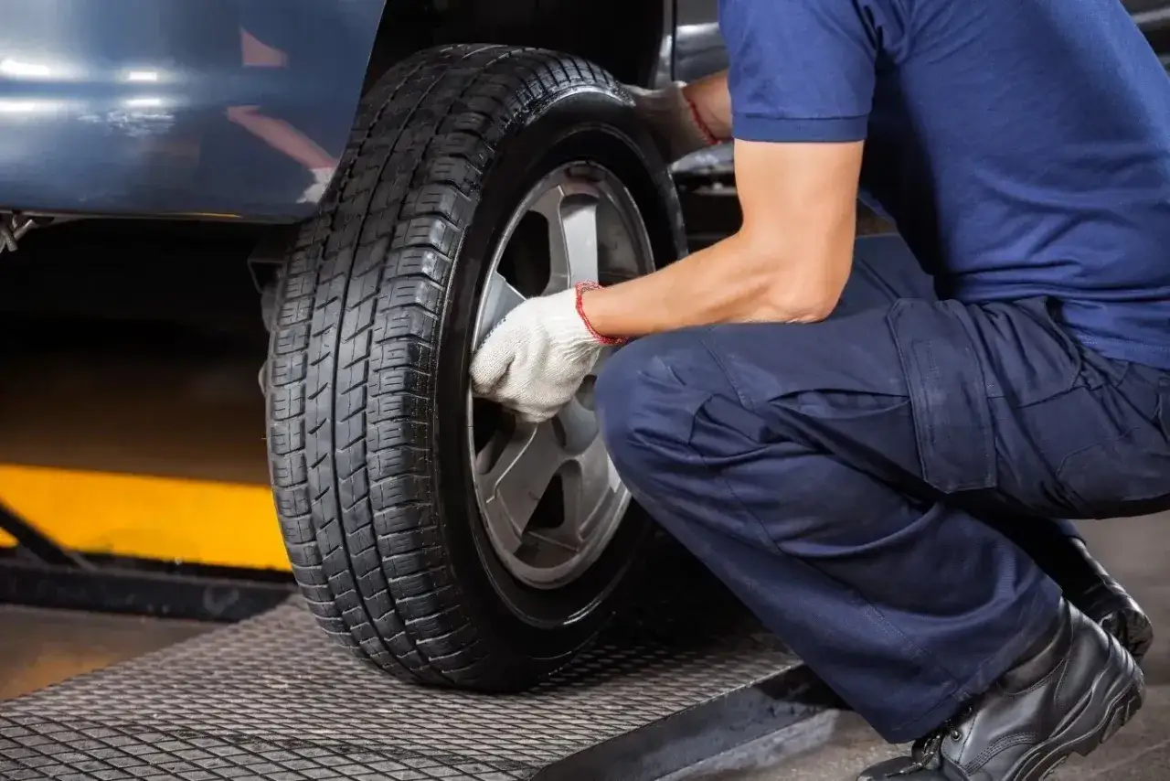 Mechanik w białych rękawiczkach dokręca śruby koła. Czas pomyśleć, kiedy wymienić opony na letnie.