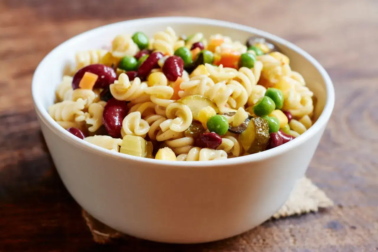 Una ciotola di pasta fredda con fagioli rossi, piselli, mais e cetriolini. Un piatto estivo perfetto.