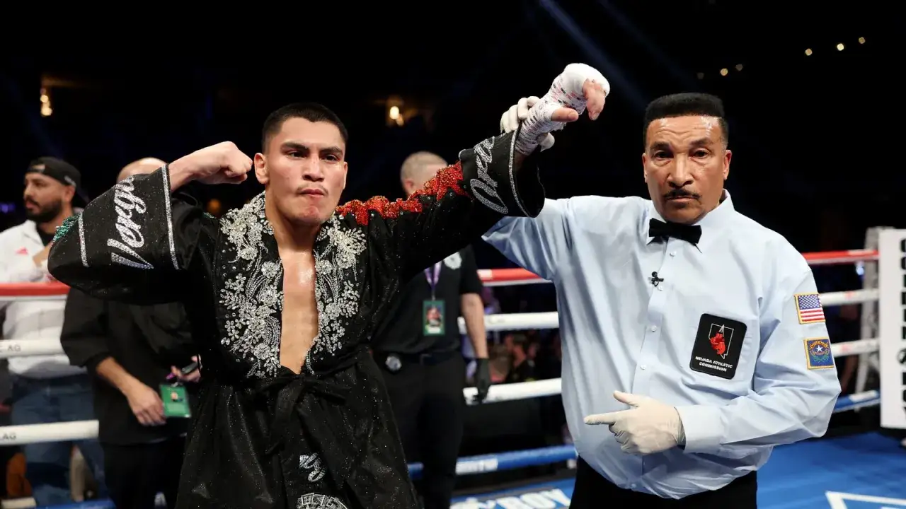 A boxer in a decorated robe has his arm raised by a referee, a moment of triumph for boxing fans.