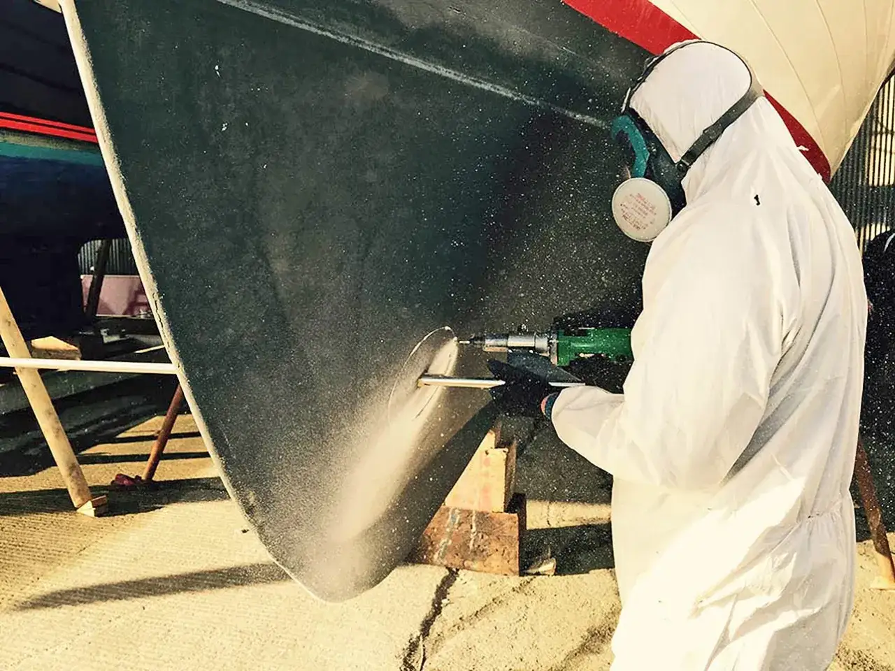 Person en combinaison blanche perce la coque d'un bateau pour installer un propulseur d'&eacute;trave.