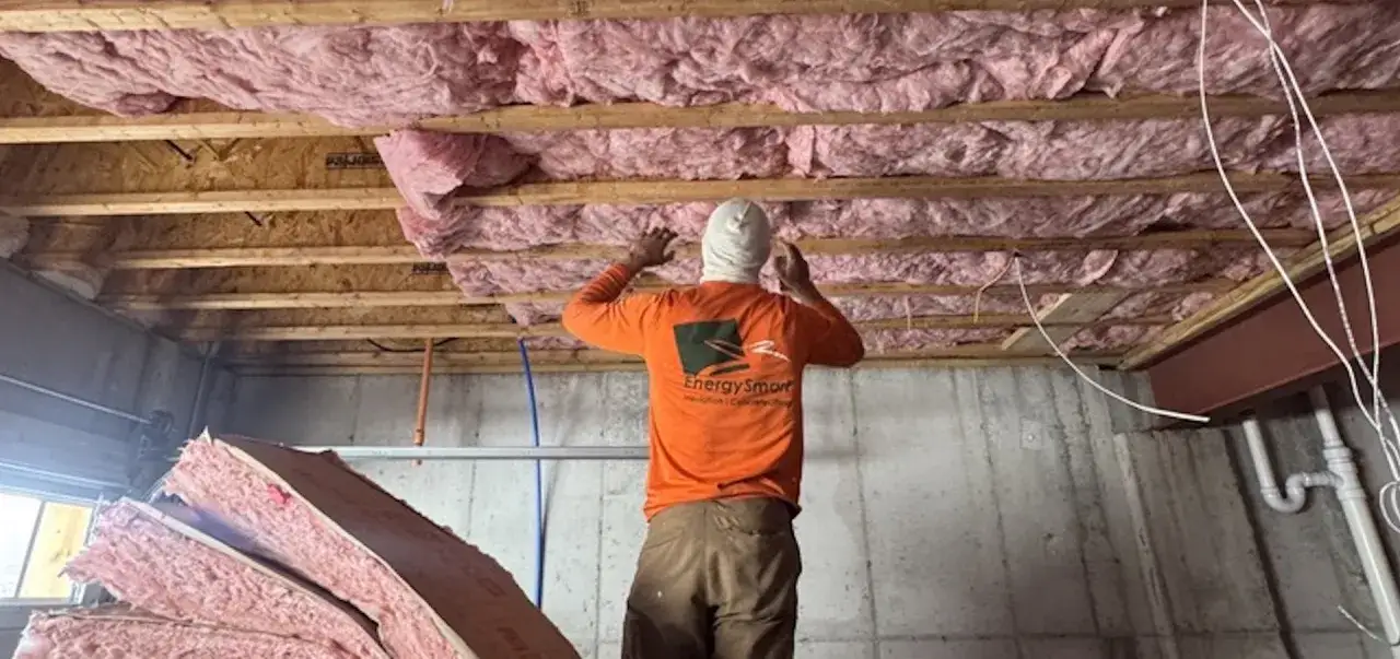 Trabajador instala aislamiento rosa entre vigas de madera, mostrando c&oacute;mo aislar una pared ya construida.